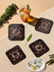A set of four black, high-gloss square coasters featuring intricate rose-gold metallic illustrations of an owl, raven, stag, and wolf framed by celestial and botanical motifs. Made from durable masonite hardboard with cork backing for slip-resistant protection.